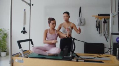 Antrenör, genç bayan müşteriyi kontrol ediyor. Spor yaparken spor yapıyor. Spor aletleri üzerinde eğiliyor.