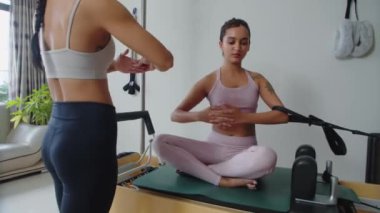 Orta uzunluktaki Asyalı antrenör, spor makinesinde çalışan bayan müşteriye egzersiz gösteriyor.