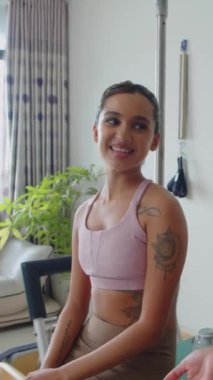 Antrenmandan sonra antrenörle konuşan Asyalı genç bir kadının dikey görüntüsü.