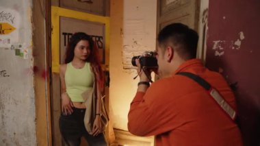 Asyalı kadın modelin eski püskü duvarın yanında duran fotoğrafçıya poz verirken orta boy bir fotoğrafı.