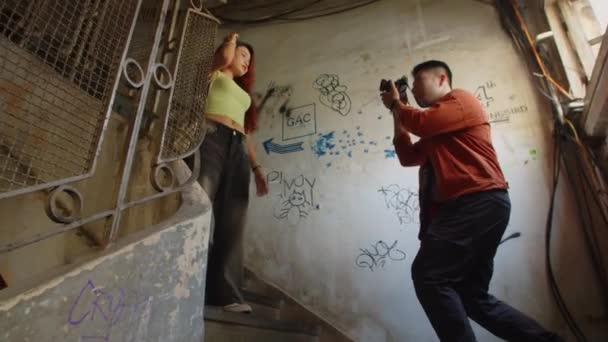 在废弃房屋内的楼梯上 年轻女性模特向男性摄影师摆姿势的角度较低 — 图库视频影像