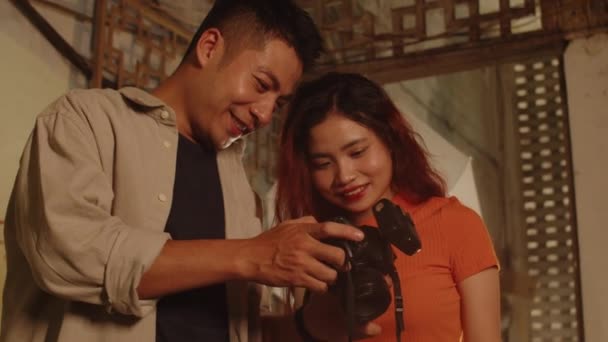 若いアジアのカップルの低い角度は 彼らが装飾された壁で放棄された建物の中のカメラで作った写真をチェックします — ストック動画