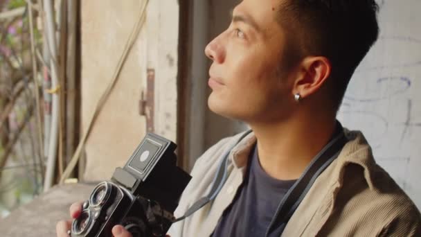 放棄された家の中の窓からのレトロカメラで撮影する男性の写真家のショットを傾倒 — ストック動画
