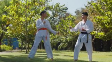 Beyaz üniformalı iki Asyalı sporcunun parkta tekvando oynarken geniş açı.