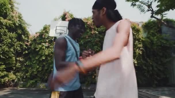 2人のアフリカ系アメリカ人のスポーツ選手が屋外でストリートボールの遊び場でお互いに挨拶 ストック映像