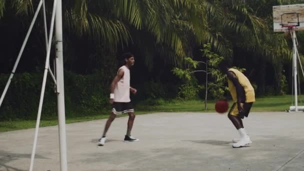 屋外裁判所でのストリートボールトレーニング中に別の選手にボールを渡すアフリカ系アメリカ人のスポーツマンのワイドショット ロイヤリティフリーのストック動画