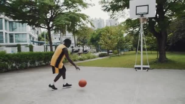アウトドアコートだけでストリートボールをする黄色いスポーツウェアの若い黒人男性アスリートのスローモーション ストック動画