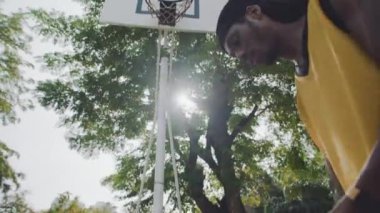 Afrika kökenli Amerikalı erkek sporcuların sokak basketbolu sahasında top oynamalarının düşük açılı görüntüsü.