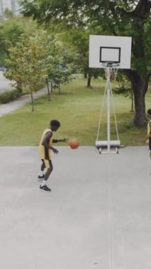 Erkek Afrikalı Amerikalı sporcuların parkta sokak basketbolu oynarken dikey çekimi.