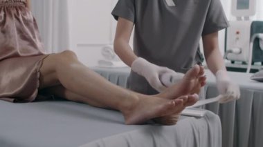 Kuaförde kadın hastaların bacaklarında tüy dökücü işlem sırasında balmumu şeritleri kullanan tanınmayan güzellik uzmanının görüntüsü.