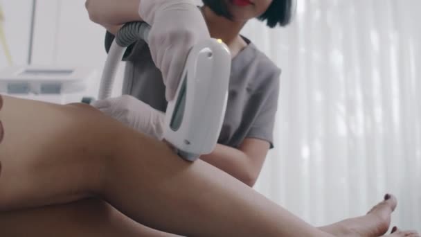クライアントにレーザーのエピレーション治療を与える若い化粧品学者のクロップショット脚の手順を得る ストック動画