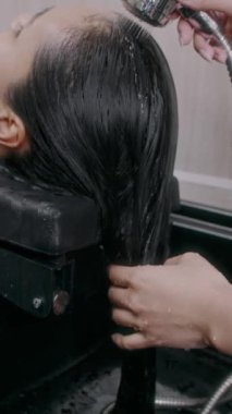 Kuaförün dikey kesilmiş elleri kaplıca salonunun lavabosundaki kadın müşteriye derin saç temizliği yapıyor.