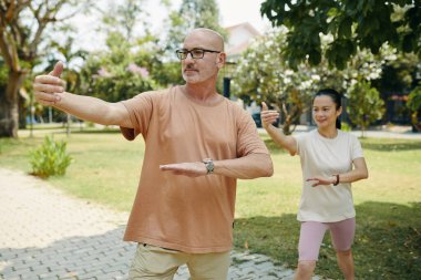 Şehir parkında tai chi yapan olgun bir çift.