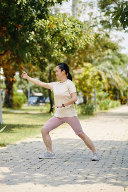 Güneşli bir sabahta parkta egzersiz yapan olgun bir kadın.