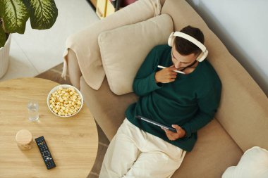 Yaratıcı genç adam tabletle kanepede oturuyor ve skeç üzerinde çalışıyor.