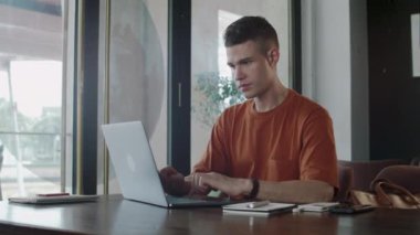 Genç Kafkasyalı iş adamının ortak çalışma alanında dizüstü bilgisayarın önünde oturduğunu gösteren orta boy bir fotoğraf.