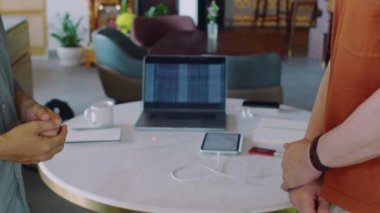 Erkek girişimcilerin kafede el sıkışırken çekilmiş görüntüsü, arka planda mali tablosu olan dizüstü bilgisayar.