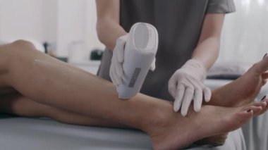 Tanımlanamayan güzellik uzmanının, balmumu kasetle kadın müşterinin bacaklarını ağdalayan görüntüsü.