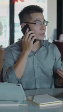 Asyalı erkek yöneticinin ofiste çalışırken akıllı telefondan müşteriyi aramasının dikey görüntüsü