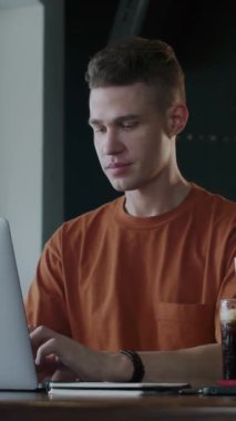 Kafede dizüstü bilgisayarla çalışırken kameraya gülümseyen genç işadamının dikey portresi