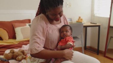 Genç siyahi annenin bebeğini kucağında tutarken evde birlikte vakit geçirirken çekilen pozu.