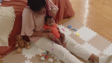 Afro-Amerikan ırkının sevgi dolu anasının bebek kızının kafasını okşaması ve yerde çıngırakla oynaması.