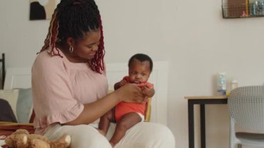 Orta boy, sevimli Afro-Amerikan bebeğinin evde annesinin ellerinde esnemesi.