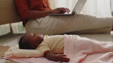 Anne evde kablosuz bilgisayarla uğraşırken yeni doğmuş bebek yastıkta kestirirken yan görüş.