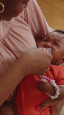 Afrikalı Amerikalı annenin ağlayan bebeğe emzik verirken dikey çekimleri.