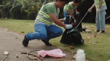 Zombi Asyalı gencin şehir parkında arkadaşlarıyla gönüllü çalışırken çöp torbasına çöp koyarken görüntüsünü kaldır.