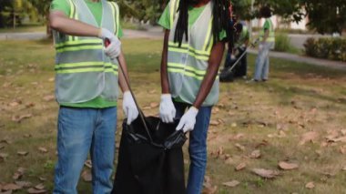 Şehir parkındaki çöpleri temizleyen ve kameraya gülümseyen iki melez gönüllünün portresini kaldır.