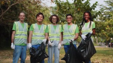 Şehir parkında çöp toplayan çeşitli gönüllülerin orta uzunluktaki grup portresi. Kamera önünde poz veriyorlar.
