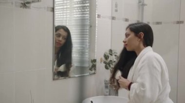 Banyoda aynanın önünde fırçalayan esmer saçlı genç bir kadın.
