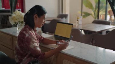 Asyalı iş kadını çalışma programı planlarken yan görüntüsü Kafe 'de dizüstü bilgisayarın önünde oturuyor.