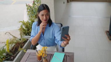 Asyalı kadın blogcunun açık kafede kahvesini içerken akıllı telefondan selfie çekerken yüksek açılı görüntüsü.