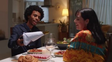 Orta boy, evde romantik bir akşam yemeği sırasında kırmızı şarabı karısının bardağına döken Afrikalı bir Amerikalı kocanın fotoğrafı.