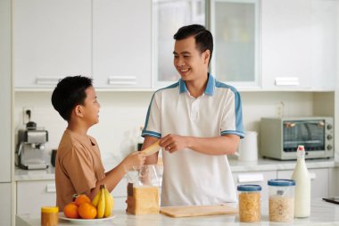 Gülümseyen Vietnamlı baba ve oğul mutfakta kahvaltı için sandviç yapıyorlar.