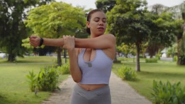 Genç Latin kadının dışarıda tek başına antrenman yaparken kol ve vücut kaslarını esnettiği orta boy bir fotoğraf.