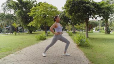 Yaz sabahı şehir parkında çalışırken İspanyol bir kızın bacak hareketlerini çekmesi.