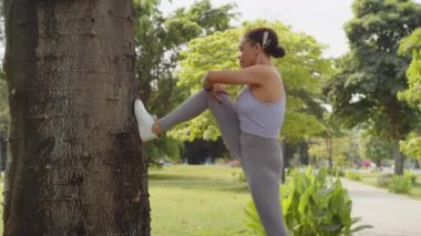 Parkta spor yaparken bacaklarına egzersiz yaptıran Latin bir kadının yan görünüşü.