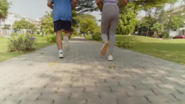 Güneşli bir havada şehir parkında koşan ve maratona hazırlanan iki sporcunun alçak açılı çekimini izliyorum.