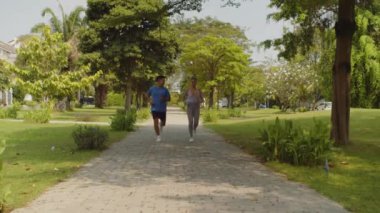 Güneşli bir sabahta şehir parkında koşan iki sporcunun statik çekimi.