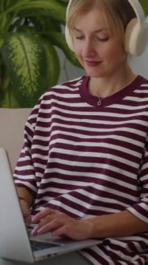 Bilgisayarda çalışan ve evde müzik dinleyen pozitif kadın serbest çalışanın dikey çekimi.