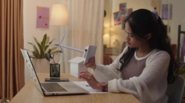 Z jenerasyonu ekoloji fakültesi öğrencisinin ev ödevi yaparken rüzgar türbini modelini tutarken, evdeki kablosuz bilgisayarın önünde otururken yan görüntüsü