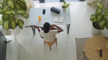 Evdeki masada oturan siyah bir kadının şarkı yazarken gitar çalması görüntüsünün hemen üstünde.