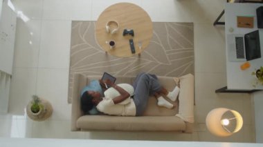 Z jenerasyonundaki Afro-Amerikalı kadının oturma odasındaki rahat koltukta dinlenirken tablet bilgisayar kullanırken görüntüsünü yakınlaştırın.