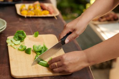 Açık havada yemek pişirirken yeşil dolmalık biber kesen kadının yakın plan fotoğrafı.