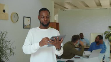 Modern başlangıç ofisinde kameraya bakarken elinde tablet olan Afrikalı Amerikalı erkek müdürün orta boy portresi