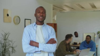 Siyahi özgüvenli erkek CEO 'nun portresi başlangıç ofisinde arka planda geliştirici ekibiyle poz veriyor.