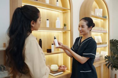 Gülümseyen güzellik uzmanı sprey toner şişesini gösteriyor.